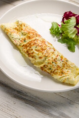 omelette breakfast on a white plate with mix salad on white wooden table vertical