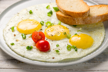Fried eggs with tomatoes, toasts and green onion on white wooden table macro close up