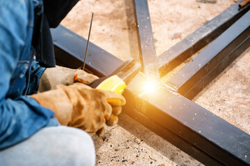 Steel welders welding large warehouse roof steel structures with electric welding tools.