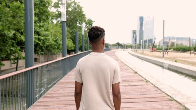 Back view of unrecognizable hispanic latino teenager boy walking alone outdoor in city street. Slow motion high quality 4k footage. Youth, success and confidence concept