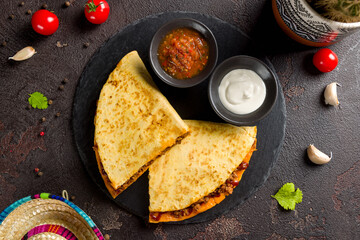 Quesadilla with beef, cheese, bbq sauce and sauces on dark stone plate top view
