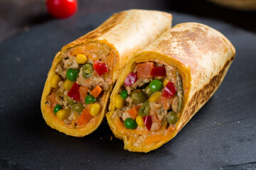 Mexican chicken burrito with spices, vegetables and cheese on black stone plate macro close up