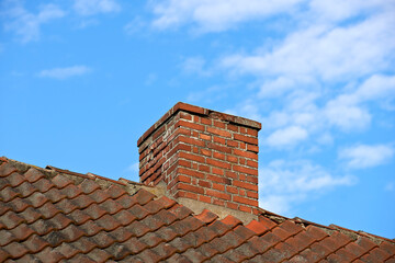 Red brick chimney designed on slate roof of a house building outside with blue sky background and copyspace. Exterior construction architecture of escape chute on rooftop for fireplace smoke and heat
