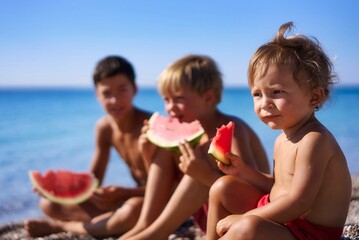 Two brothers eat a watermelon on the beach