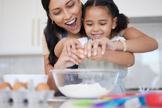 Young mother enjoying baking, bonding with her little daughter in the kitchen at home. Little latino girl smiling while helping her mother cook a meal at home. Child cracking an egg for a recipe