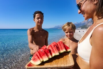 Two brothers eat a watermelon on the beach