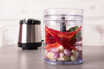 Garlic, shallots, pieces of red chili, and various other spices are placed in the electric food chopper container, before being pureed. The driving machine is behind it.
