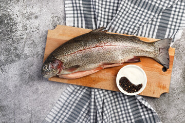 Raw rainbow trout on a cutting wooden board on a dark grey background. Top view, flat lay
