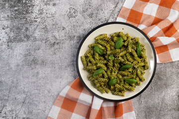 Fusilli pasta with Spicy Pesto and fresh basil leaves on a round plate on a dark gray background....