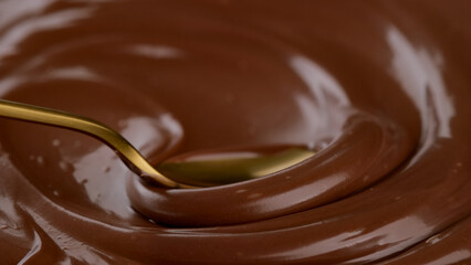 Hand stirring melted dark chocolate with golden spoon, close up. Confectioner prepares chocolate dessert, glaze