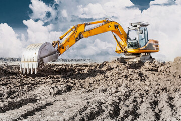 A powerful excavator digs the ground against the blue sky. Earthworks with heavy equipment at the...
