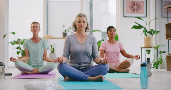 Mature women meditating in lotus pose in zen yoga class. Diverse group of yogis sitting together on mats, legs crossed, finding inner mental balance and peace. Practising calming breathing exercises