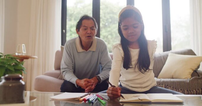 Grandfather bonding with his granddaughter as she draws a picture in a coloring book. Happy girl doing her homework and bonding with her grandpa during a visit. Man helping a child study