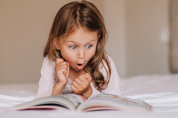 Emotional child girl read interesting book in bed. Small kid enjoy reading. Fantasy and fantastic. Developing child fantasy and imagination. Imaginary world. Fairy tale. Bedtime reading