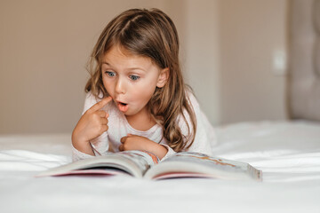 Fantasy literature. Emotional child girl read interesting book in bed. kid enjoy reading. Fantasy and fantastic. Developing child fantasy and imagination. Imaginary world. Fairy tale. Bedtime reading
