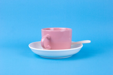 A pink cup of coffee on wjite dish and blue color background