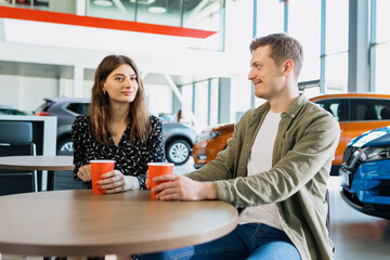 Fototapeta premium Buying a family car. The couple drinks coffee at the table while the paperwork for the car is being processed