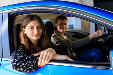 A young family is sitting in a new car at a dealership. A young woman looks at the camera