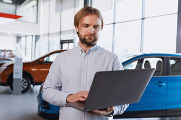 A car dealership employee with a laptop stands in the background of the showroom