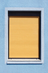 Fenster mit braunen heruntergezogenen Rolläden an einer blauen Hauswand, Deutschland