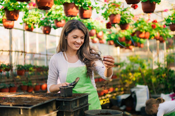 Smiley woman in 30's checking quality of earth for filling the pots she need for flowers from greenhouse.