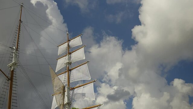 Masts with sails of a large ship against the background of clouds in the blue sky. The ship is moored on the river Danes in Klaipeda. Warm summer sunny day in Lithuania.