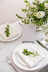 Mockup white blank space card for table number or menu. Wedding teble decoration with white flowers, glasses and white napkins. Elegantly decorated table at a wedding reception. 