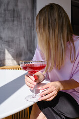 A glass of red wine, champagne or a cocktail in the hands of a girl relaxing in a restaurant. Tasting of alcoholic beverages. Summer rest. Romantic evening aperitif. Close-up of a glass of wine