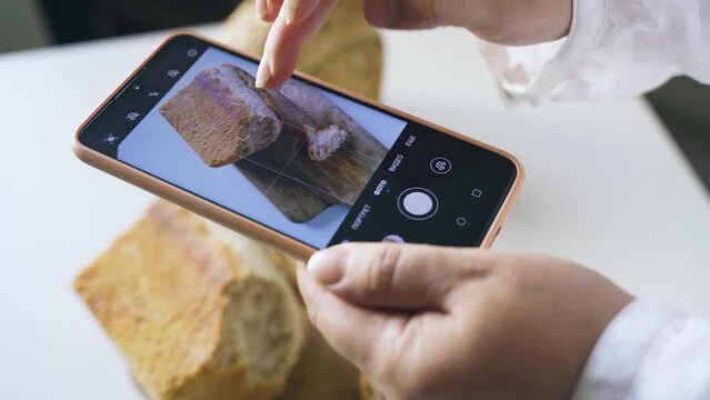 A woman shoots homemade bread on her phone. Bread lies on a wooden board. Takes a photo for a social network
