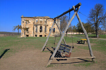 Fototapeta premium Wooden swing against the backdrop of an old abandoned estate.