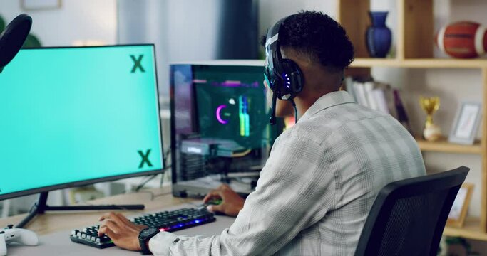 Young guy streaming an online multiplayer game on his desktop computer with the latest operating system. Serious gamer playing a video game on green screen monitor with a headset.