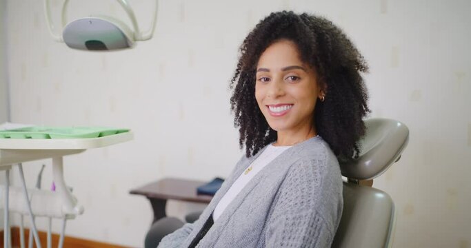 Portrait of woman happy with dental treatment, smiling sitting in a dentist chair in a consultation office. Black woman excited to have her teeth cleaned, satisfied with her veneers