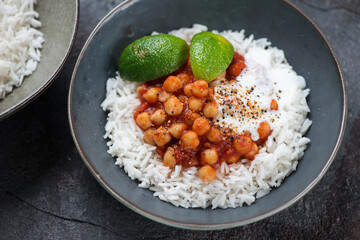 Grey bowl with chana masala or curried dish with chickpeas, onions, tomatoes, spices and herbs over basmati rice, close-up, studio shot