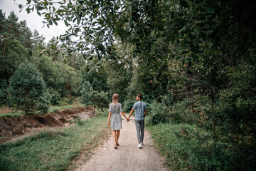 Fototapeta premium A guy and a girl holding hands are walking in the spring forest