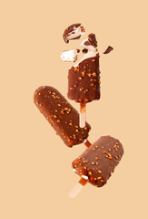 white popsicle in chocolate glaze with nuts flying on a beige background, selective focus
