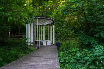 White pavilion and wooden walkway in public park with trees in summer