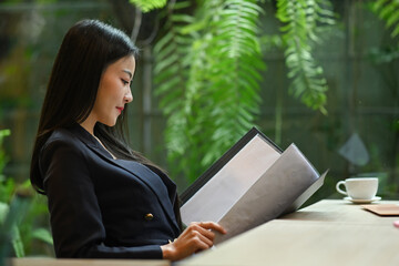 Beautiful millennial businesswoman reading document in office with nature view in background