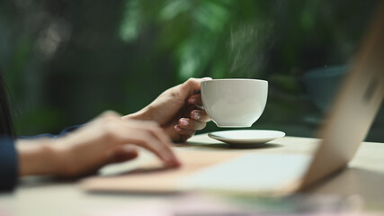 Cropped image of young woman hand holding cup of hot coffee with natural morning background
