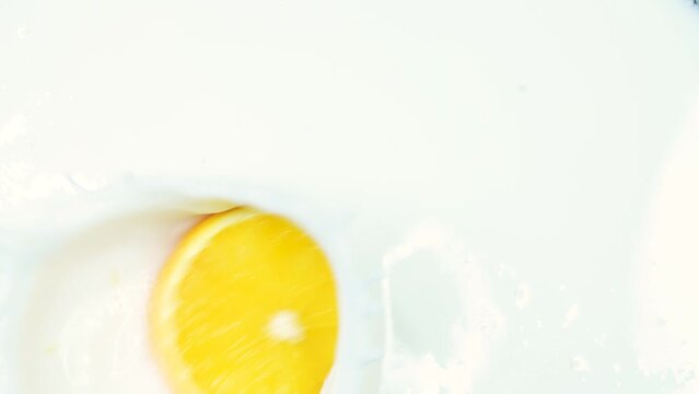 Slice of fresh orange falling into milk