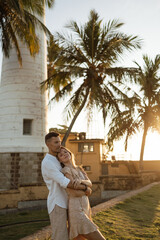 Fototapeta na wymiar Happy European couple in love hugging, kissing and enjoying the company of a friend against the backdrop of the lighthouse in Galle Fort. Valentine's Day.