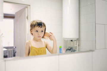 Cute toddler baby combs in front of bathroom mirror