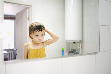 Cute toddler baby combs in front of bathroom mirror