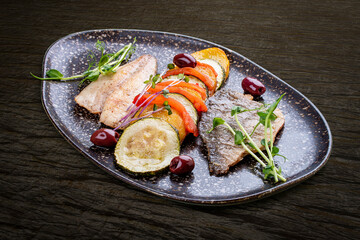 Sea bass fillet with vegetables ratatouille . On dark background, isolated. - obrazy, fototapety, plakaty