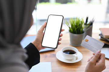 Over shoulder view of Muslim woman holding credit card and using mobile phone. Online shopping, internet banking concept