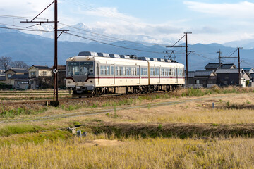 雪をいただく山を背に、のどかな田園風景の中を走る富山地方鉄道の電車