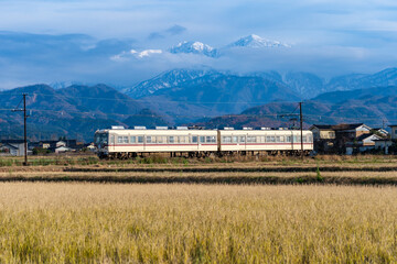 雪をいただく山を背に、のどかな田園風景の中を走る富山地方鉄道の電車