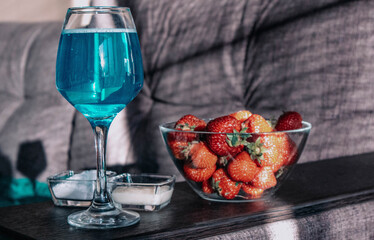 A glass of champagne gives shade on the couch. Champagne in a glass and strawberries stand on a wooden mini table top