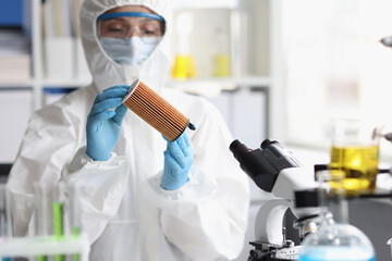 Woman in protective respirator and white coverall researching filter in lab
