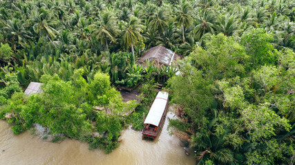 aerial top down view of boat docked at pier along brown mekong delta river coastline on jungle of...