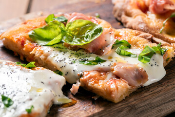 Fette di pinsa romana con prosciutto cotto, mozzarella, sugo, basilico e semi di papavero, cibo...
